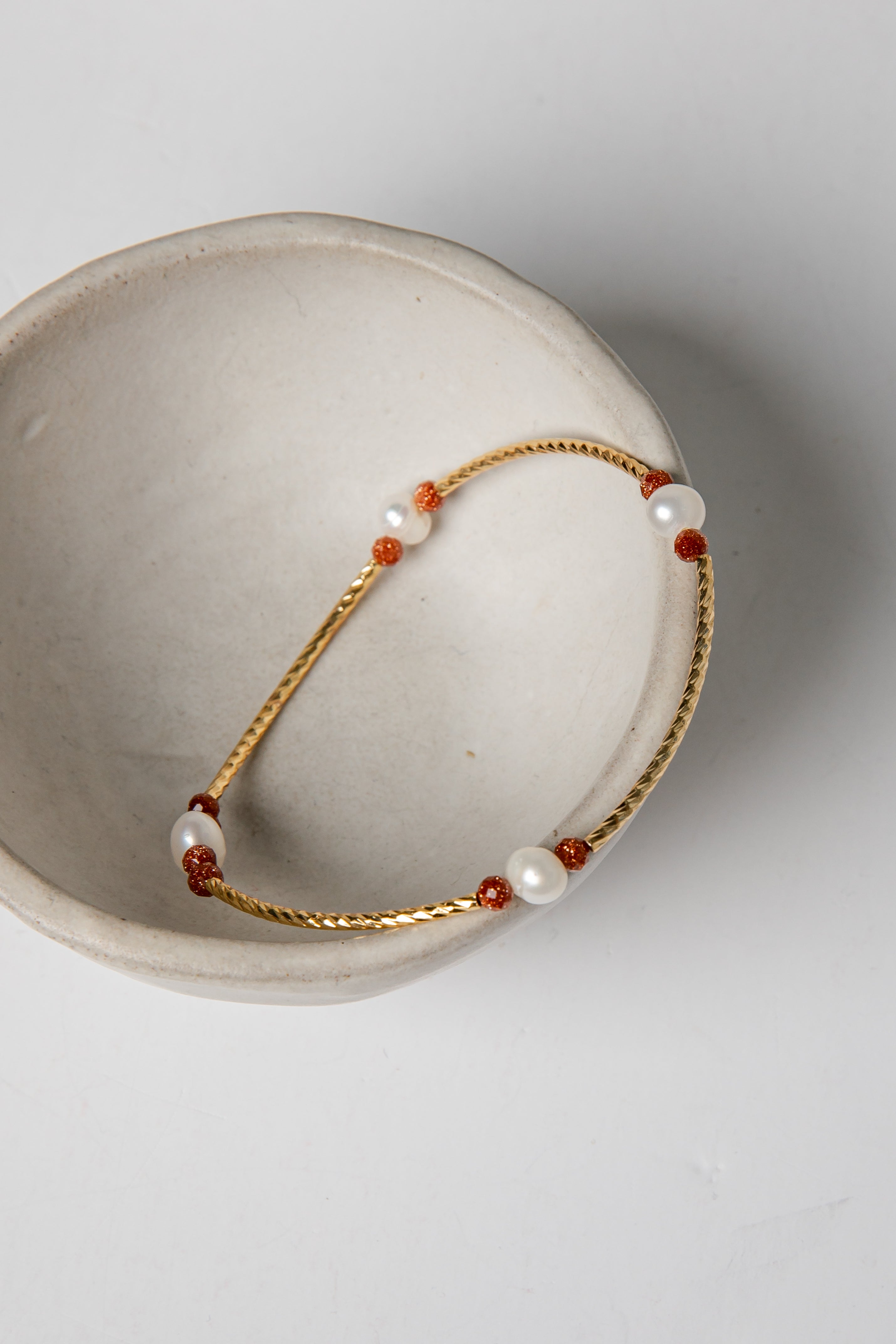 Bracelet with gold chain and red and white beads on a light gray background