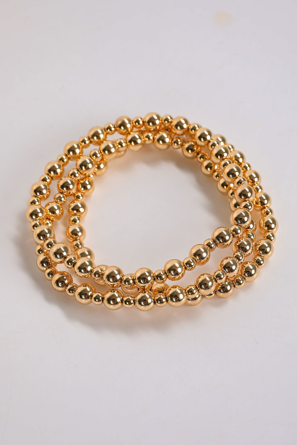 Two gold beaded bracelets on a light gray background